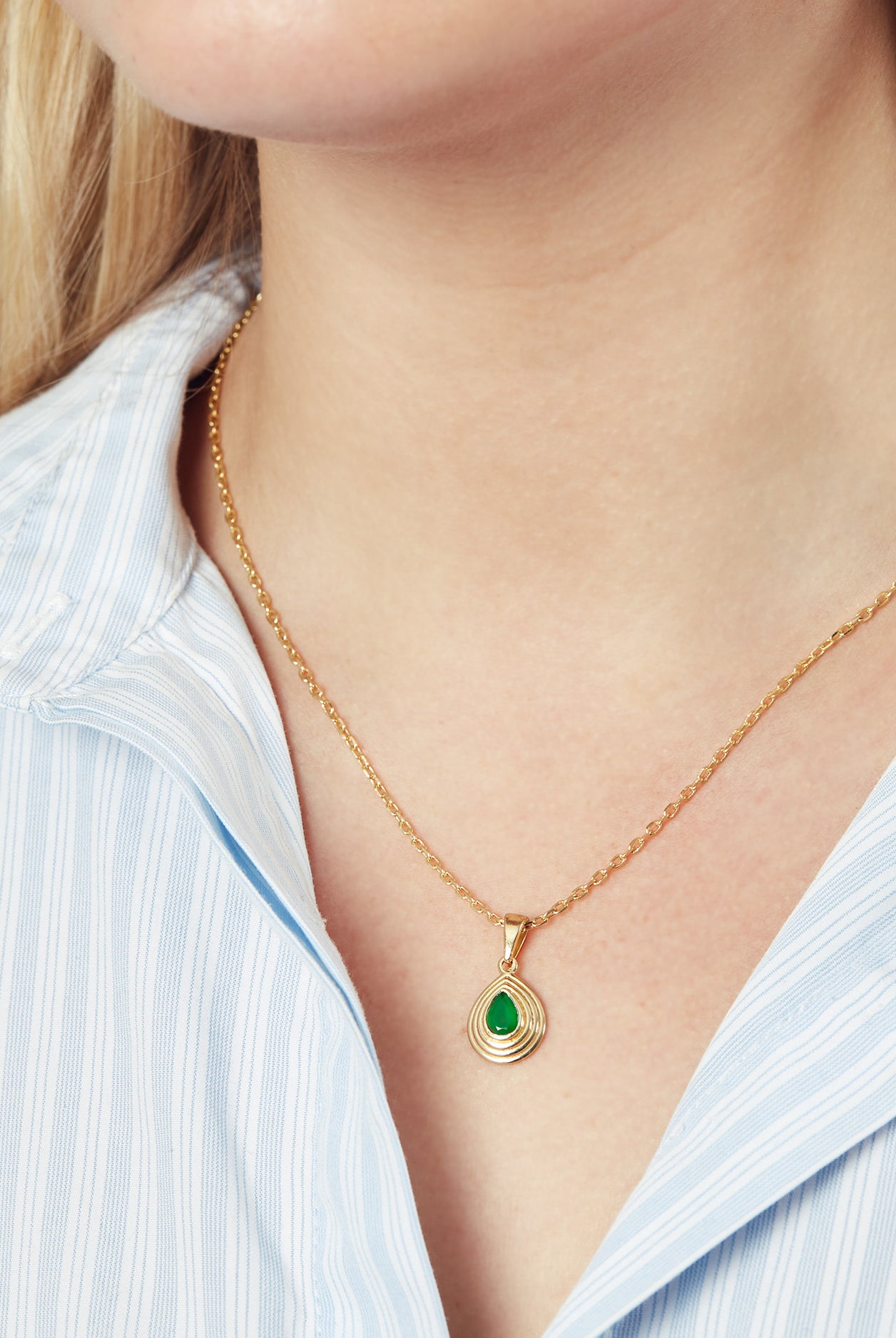 Gold chain necklace with teardrop pendant with a green onyx gemstone worn by a model wearing a blue and white shirt