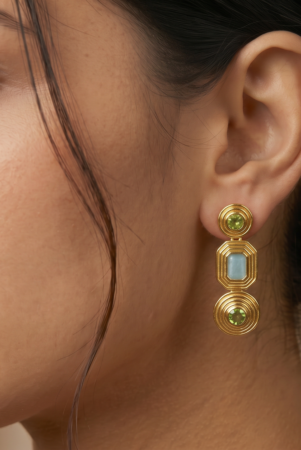 AI Image: Close-up of a woman wearing gold cascade earrings with green and light blue gemstones against a neutral background