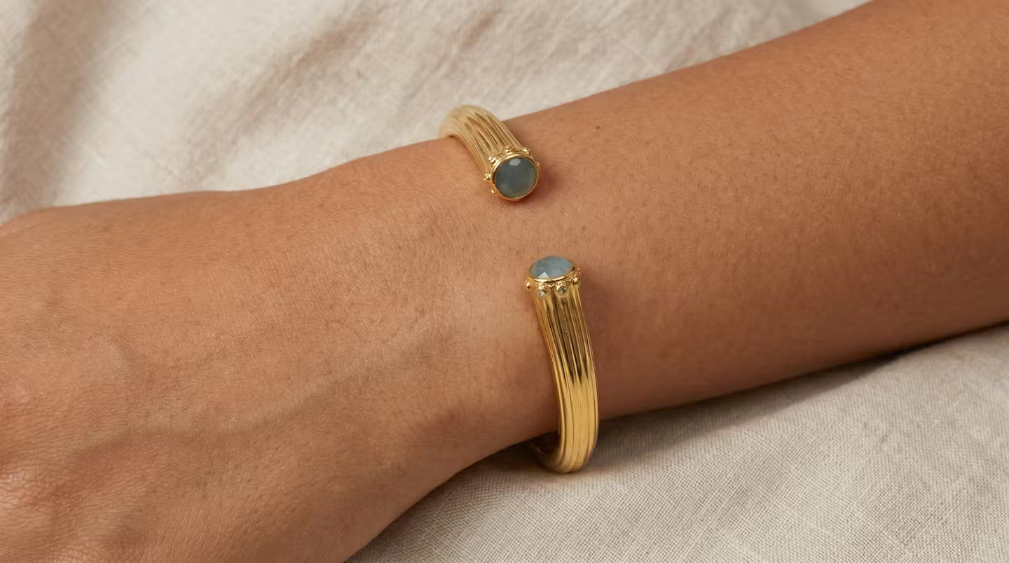 AI Image: Gold cuff bangle with light blue and green stones on a wrist against a neutral background