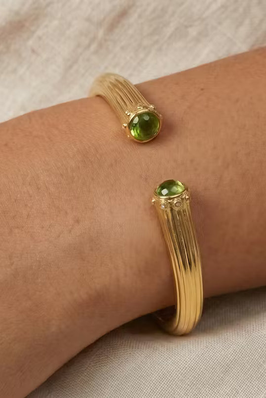 AI Image: Gold cuff bangle with green and yellow gemstones on a wrist against a neutral background