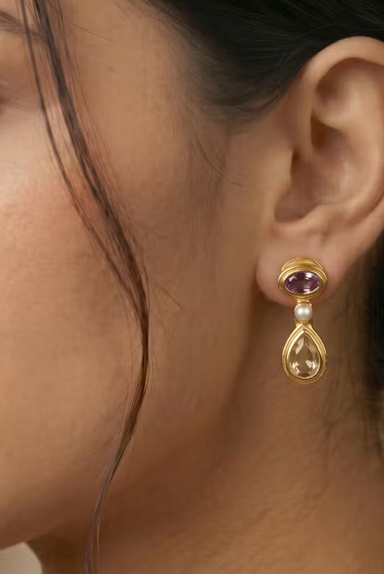 AI Image: Close-up of a woman wearing gold drop earrings with pearl, purple and yellow stones on a beige background