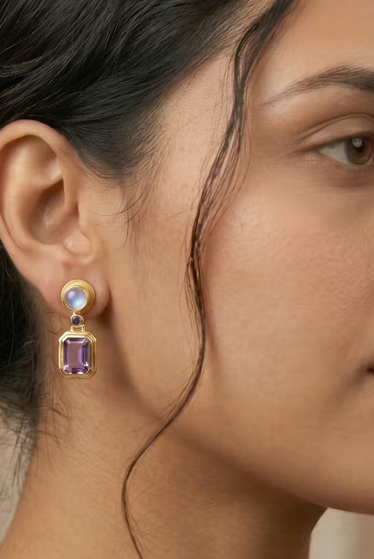 AI Image: Close-up of a woman wearing a pair of gold round and rectangular drop earrings with purple and opal gemstones on a beige background