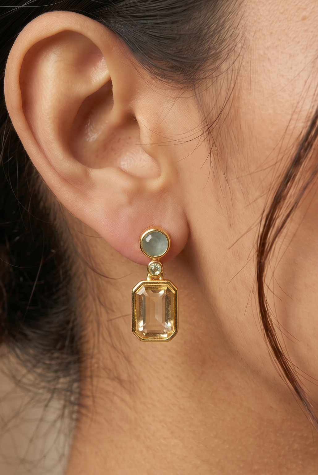 AI Image: Close-up of a woman wearing gold round and rectangular drop earrings with light blue and green gemstones against a neutral background