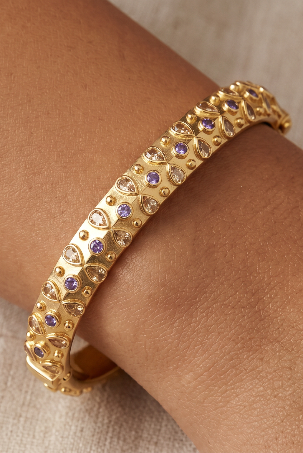AI Image: Gold bangle with purple and yellow gemstones on a wrist against a neutral background