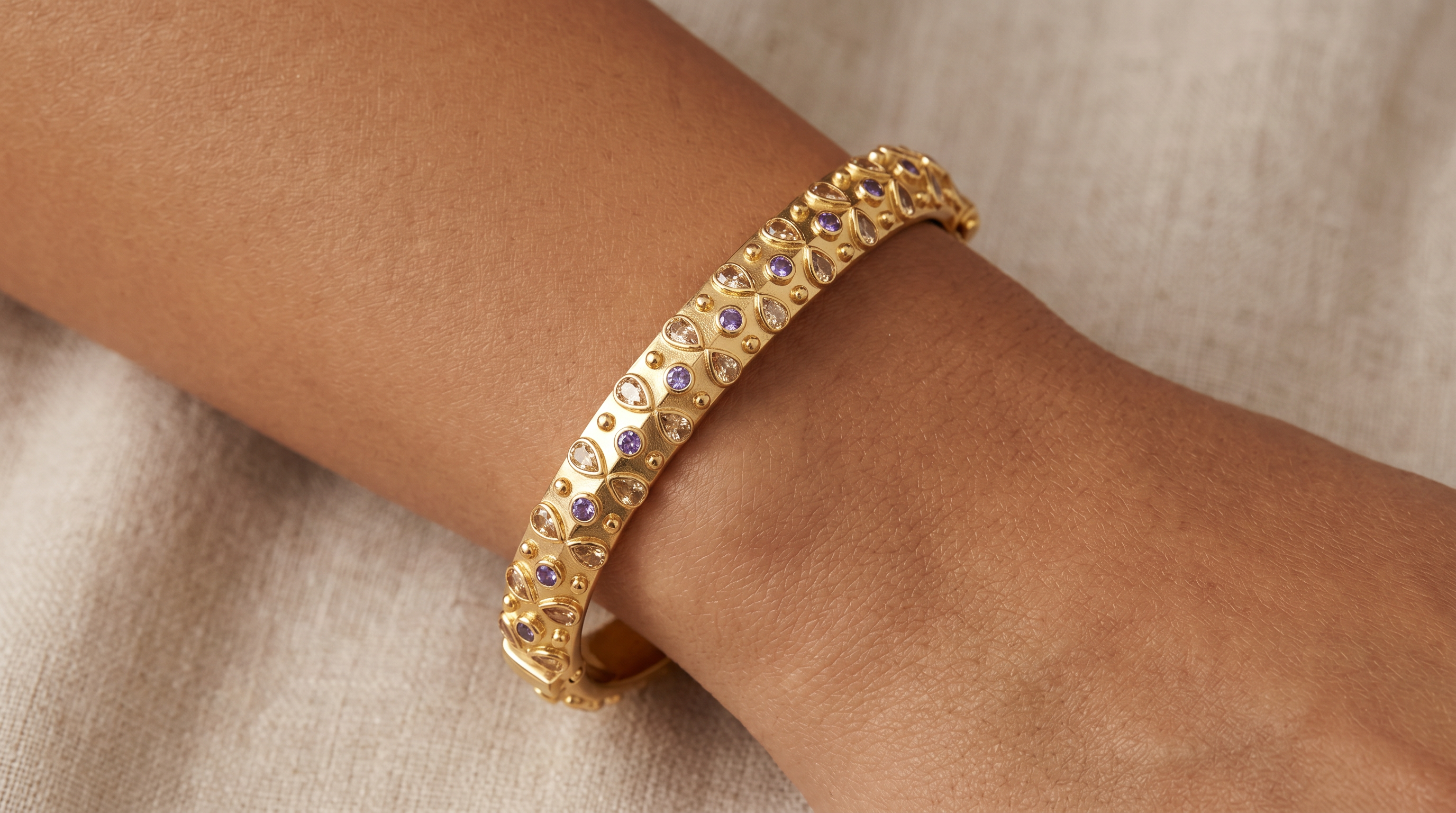AI Image: Gold bangle with purple and yellow gemstones on a wrist against a neutral background