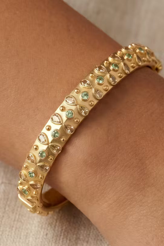 AI Image: Gold bangle with yellow and green gemstones on a wrist against a neutral background