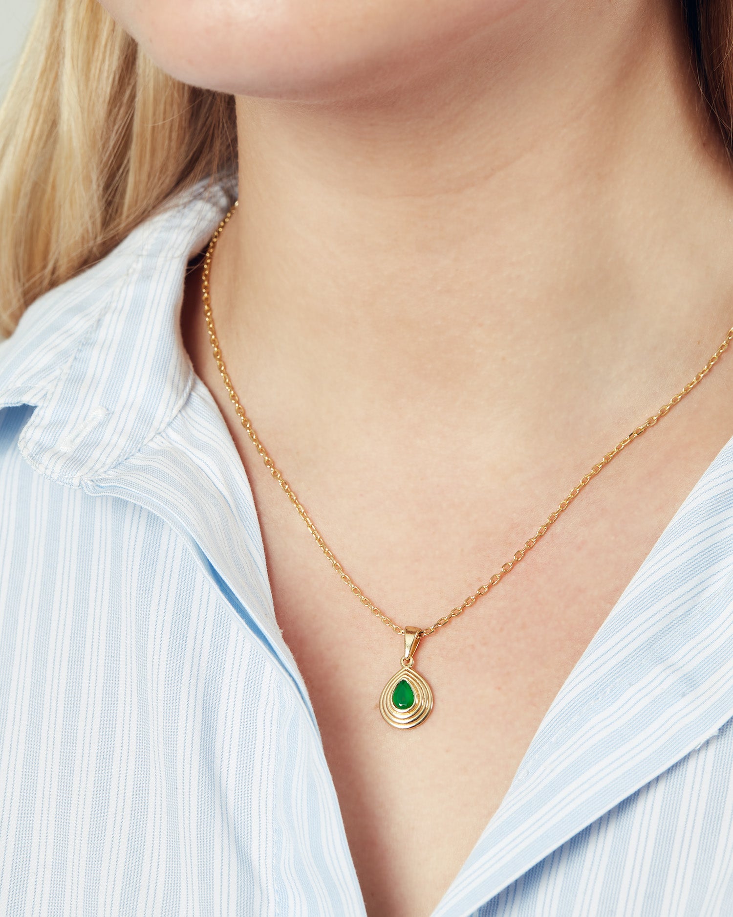 Gold chain necklace with teardrop pendant with a green onyx gemstone worn by a model wearing a blue and white shirt