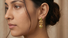 AI Image: Woman wearing gold cascade earrings with green and yellow gemstones a neutral background