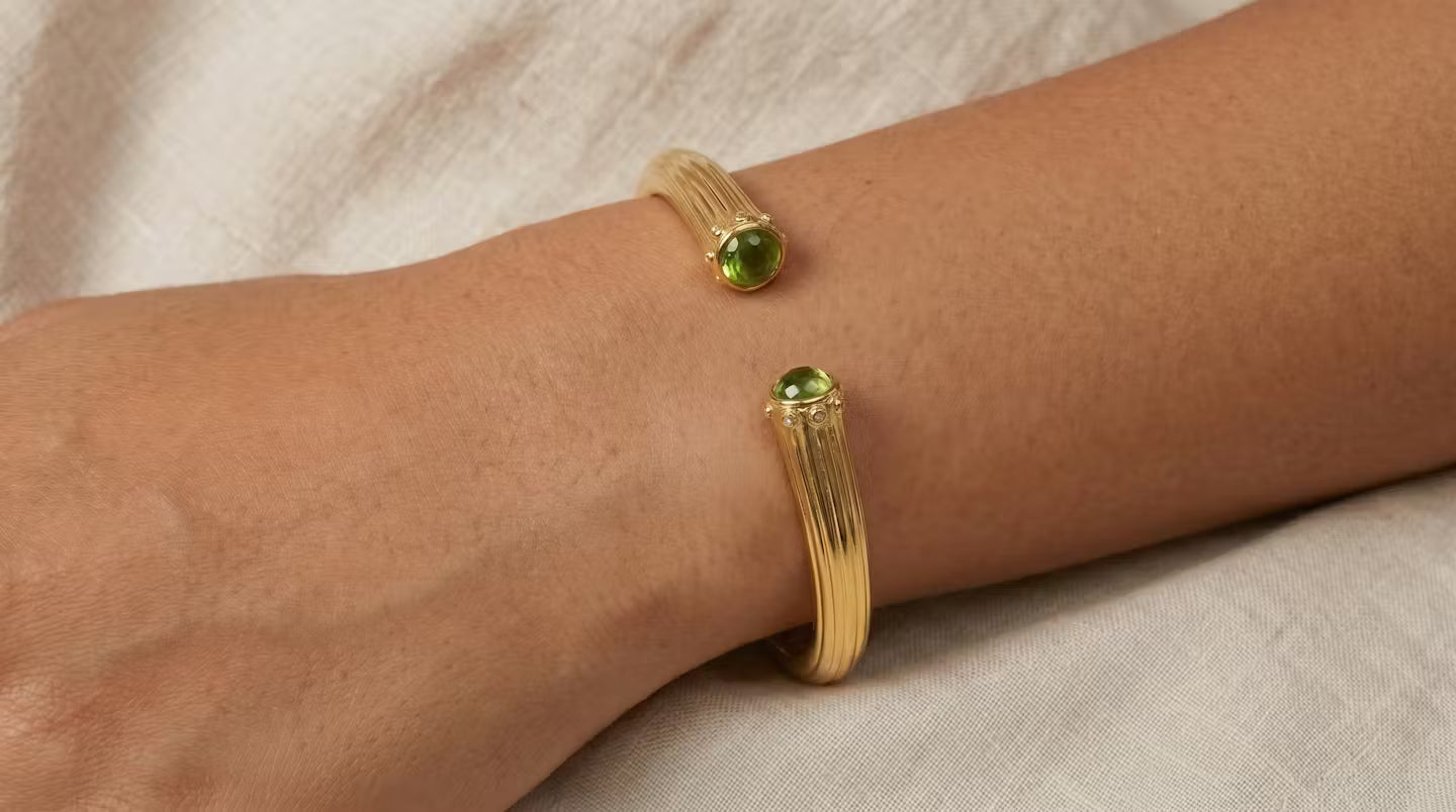 AI Image: Gold cuff bangle with green and yellow gemstones on a wrist against a neutral background