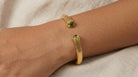 AI Image: Gold cuff bangle with green and yellow gemstones on a wrist against a neutral background