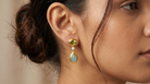 AI Image: Close-up of a woman wearing a gold drop earring with  pearl, green and light blue gemstones 