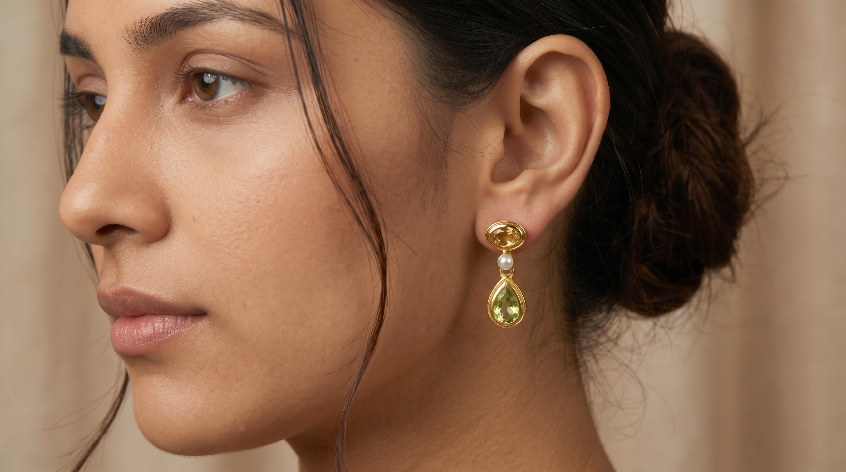 AI Image: Close-up of a woman wearing gold oval and teardrop earrings with pearl, green and yellow gemstones on a beige background