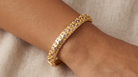 AI Image: Gold bangle with purple and yellow gemstones on a wrist against a neutral background