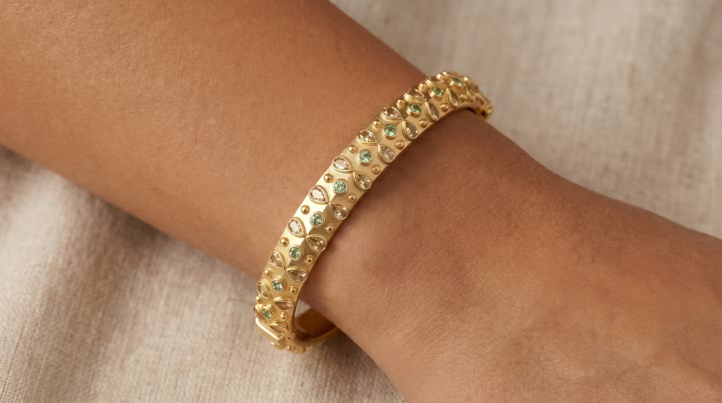 AI Image: Gold bangle with yellow and green gemstones on a wrist against a neutral background